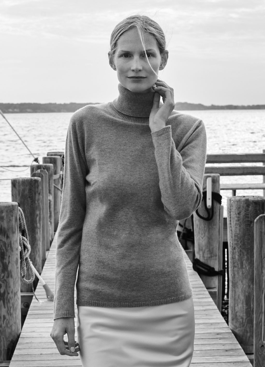 Model Katrin Thormann wearing light grey cashmere rollneck jumper on a dock by the water