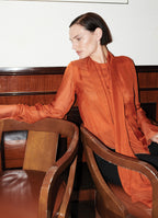Model Sophie Grace Hirsch wearing burnt orange silk bow blouse in a restaurant setting