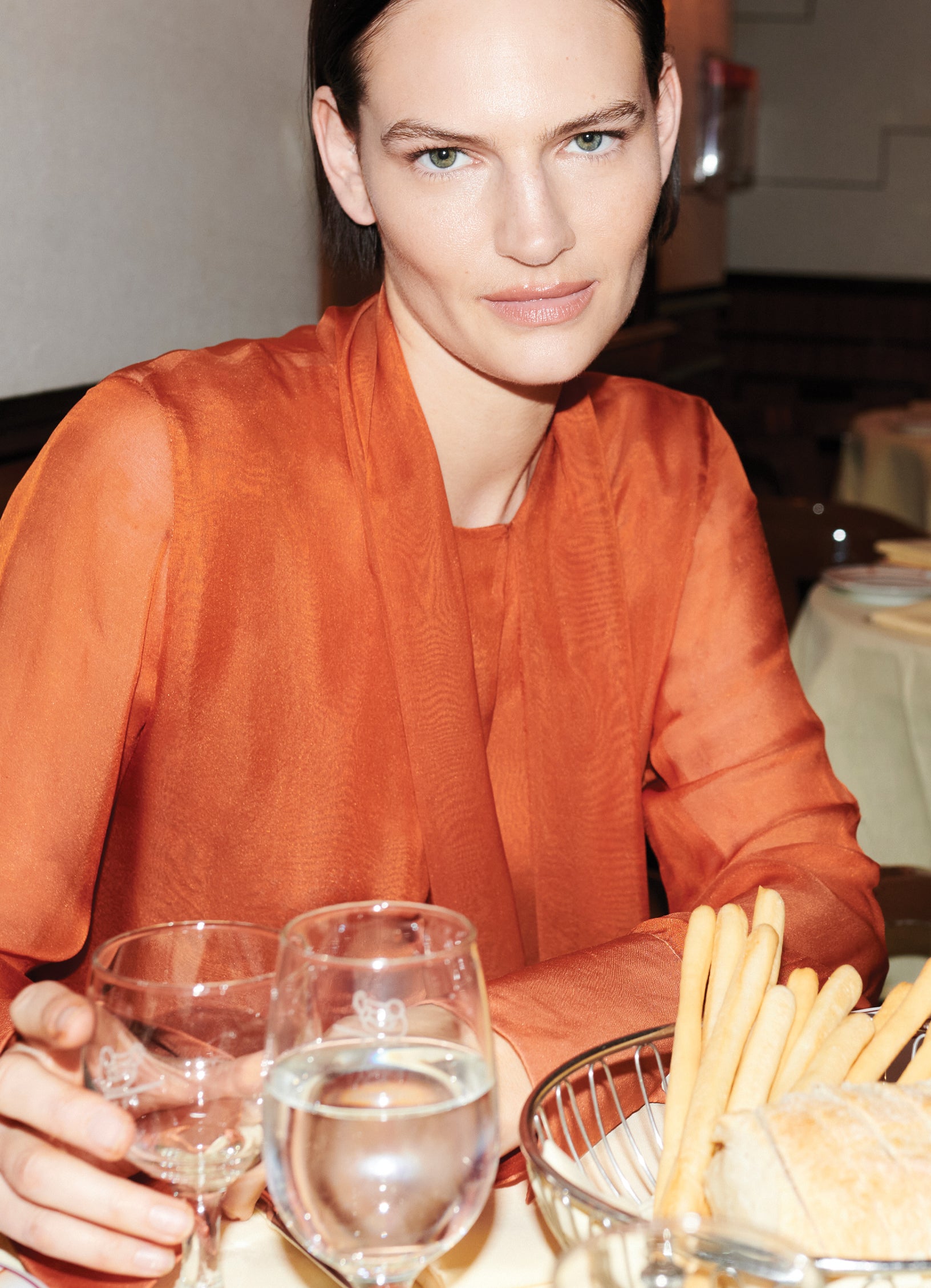 Close-up of model Sophie Grace Hirsch  wearing burnt orange silk blouse with draped tie neckline