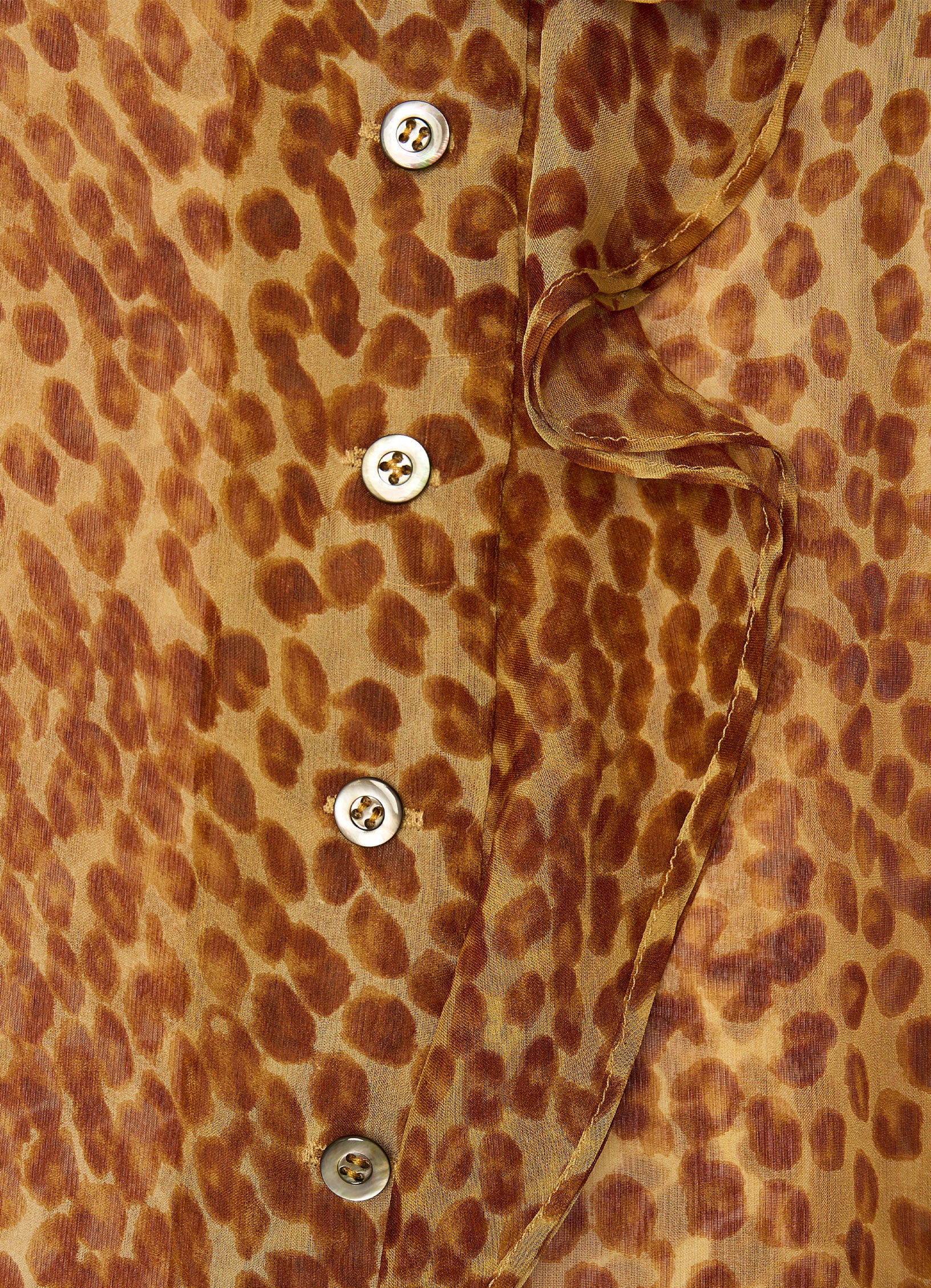 Close-up detail of shell buttons and ruffle trim on ozelot print silk blouse