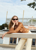Model Katrin Thormann in abstract ozelot silk blouse leaning on railing at Sunset Beach restaurant in the Hamptons