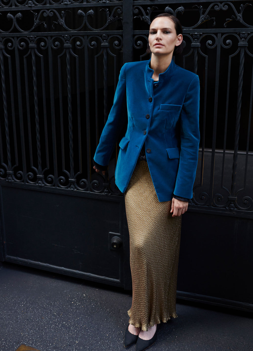 Tailored velvet jacket in petrol styled with gold skirt against black iron gate in New York City