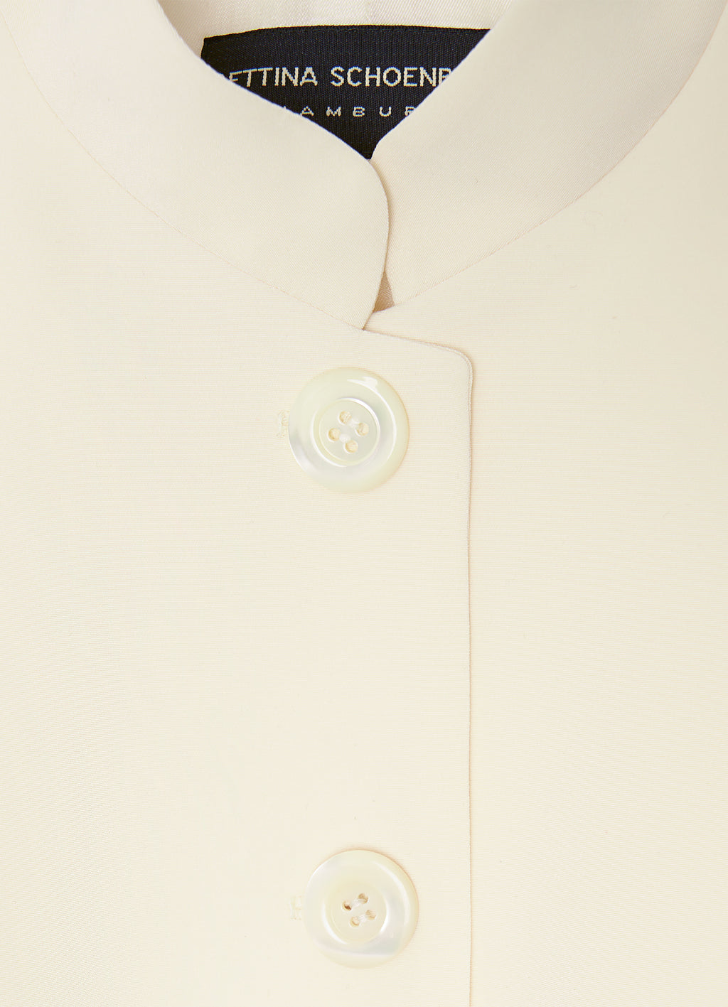 Close-up detail of the ecru vest featuring a stand collar and tonal button fastening.