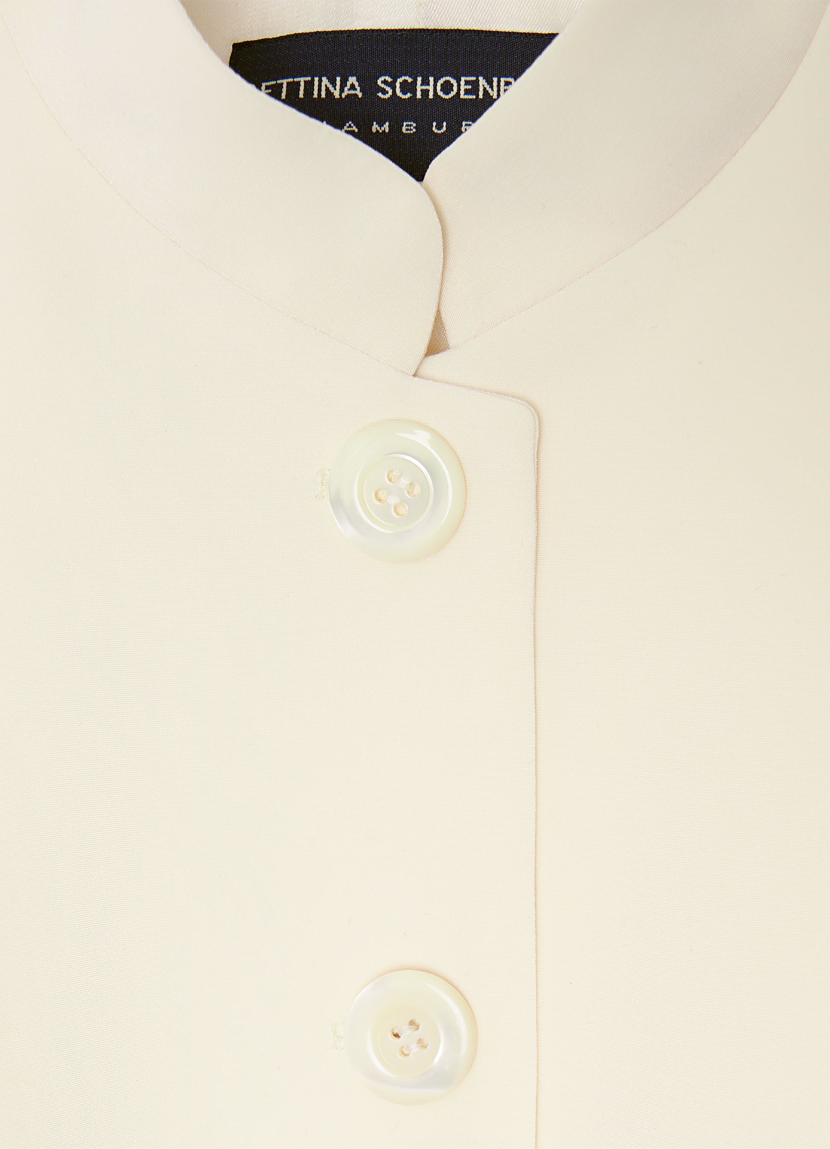 Close-up detail of the ecru vest featuring a stand collar and tonal button fastening.